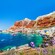 Una pequeña cala con botes pesqueros en el agua y edificios bajos construidos sobre la costa rocosa